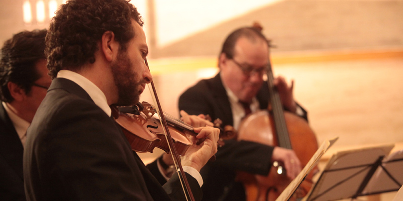 Close up of a violinist and a cellist playing. The violinist is to the left and in the foreground, and the cellist is to the left and slightly in the background.