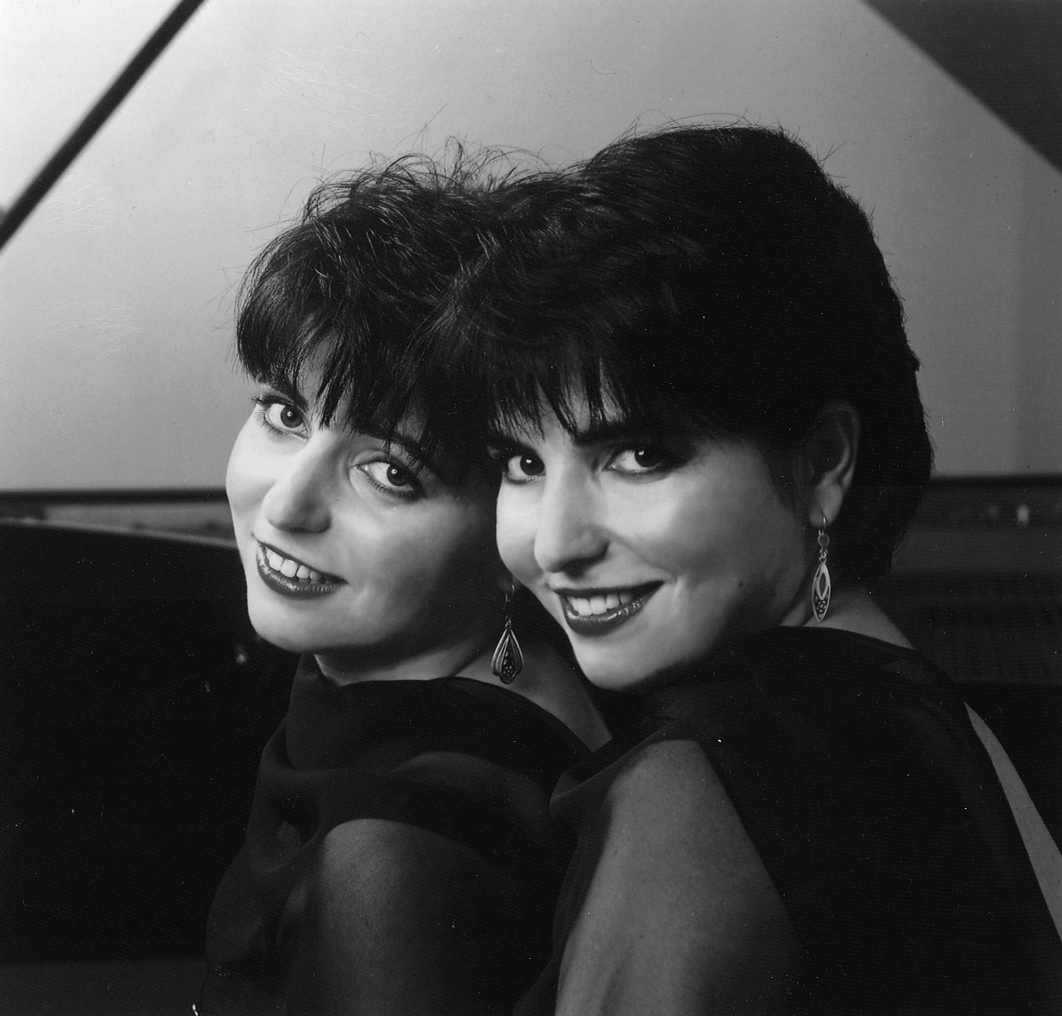 Elkina Twins smiling side by side in front of a piano